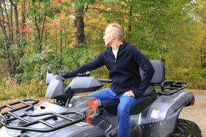 Man sitting on an ATV in a forested area wearing abode outside